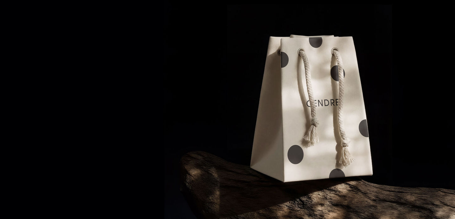 Cendre luxury home fragrance shopping bag with dark dot motif pattern and braided rope handles, photographed on weathered driftwood against a deep black background. Brand identity and packaging design by Studio Ruby Signorelli.