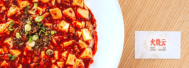 A plate of mapo tofu, a classic Sichuan dish of tofu in a spicy sauce, with ground pork and vegetables, garnished with chopped scallions.