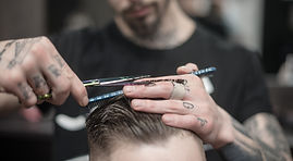 A man is getting his hair cut. The barber is using a pair of scissors and a comb to cut the man's hair.