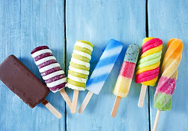 A variety of colorful popsicles against a blue wooden background in a row.