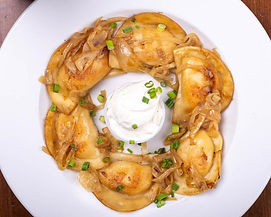 A plate of pierogis, topped with fried onions and served with sour cream.
