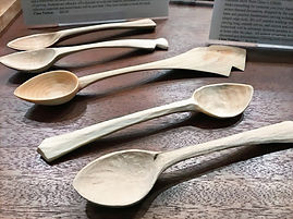 Five wooden spoons of different sizes and shapes are displayed on a dark wood table. The spoons are all handmade and have a unique design.