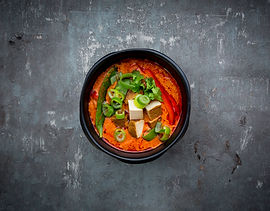 Tofu Red Curry. A bowl of red curry with tofu, peppers, and green onions sits on a gray stone surface.