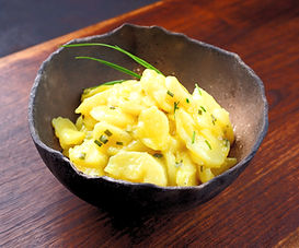 A close-up of a bowl of potato salad with chives on a wooden table.