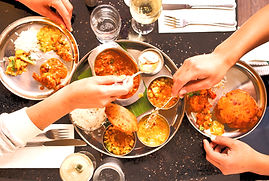 Vegetarian Thali. A group of people are eating a meal together, sharing dishes of curry, rice, and naan bread.
