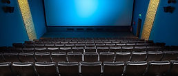 Empty movie theater with a blank screen. The theater has black reclining seats and blue walls with subtle lighting.