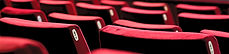 Red Theatre ChairsEmpty red theater seats are shown facing an out-of-focus stage with a twinkle of white lights.