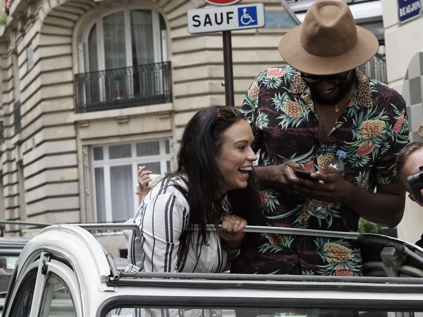 Participants in an open-top classic car on a Paris street during the programme