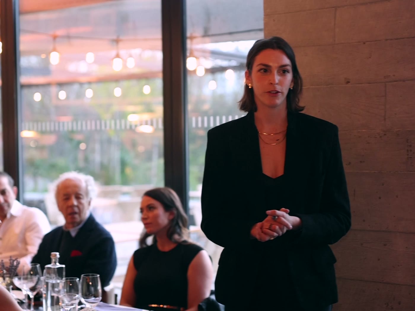 A host in a black suit addressing the seated room during the Maxim cover party