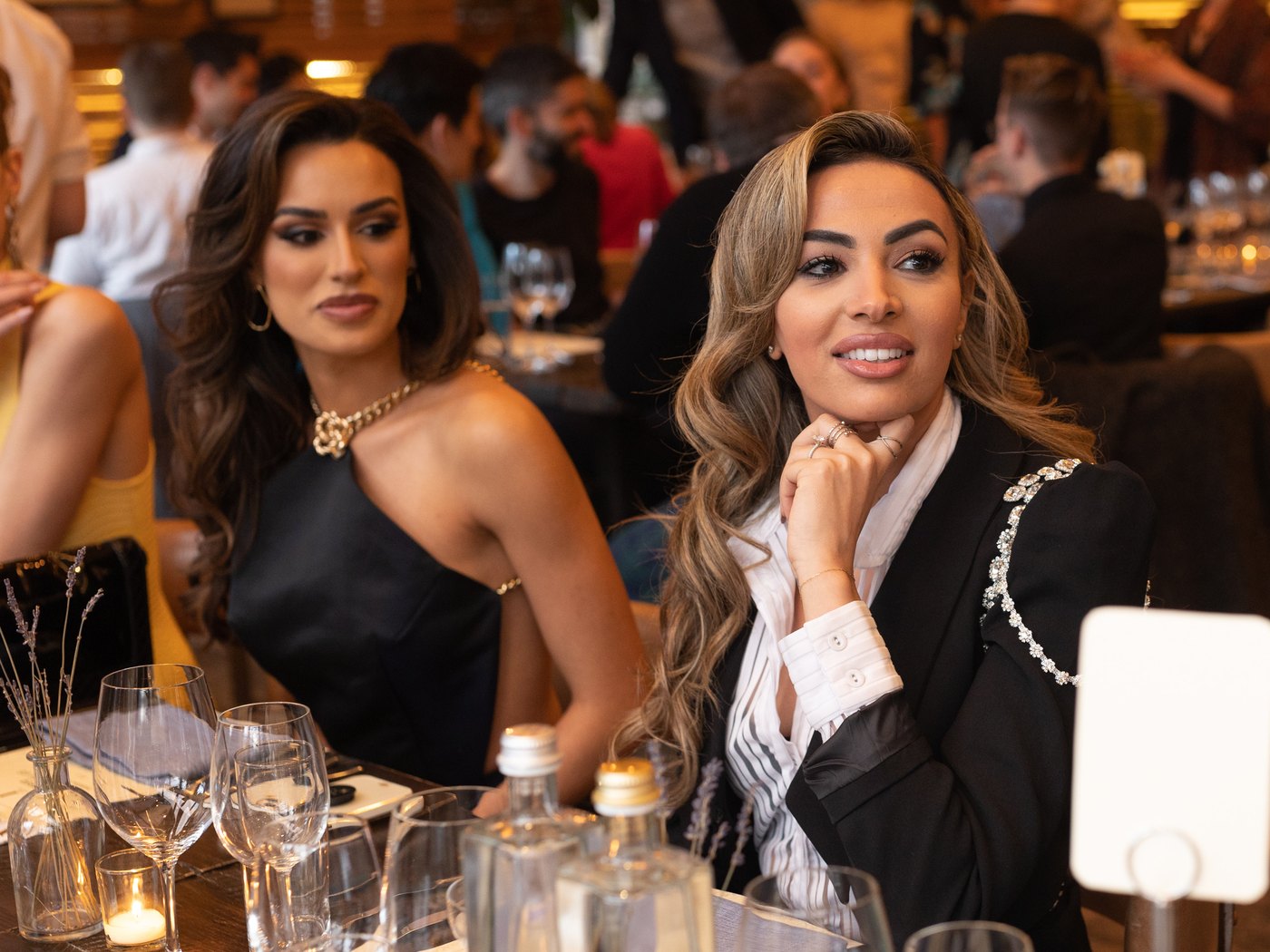 Two guests seated at the candlelit table during the Maxim cover dinner, the dining room busy behind them