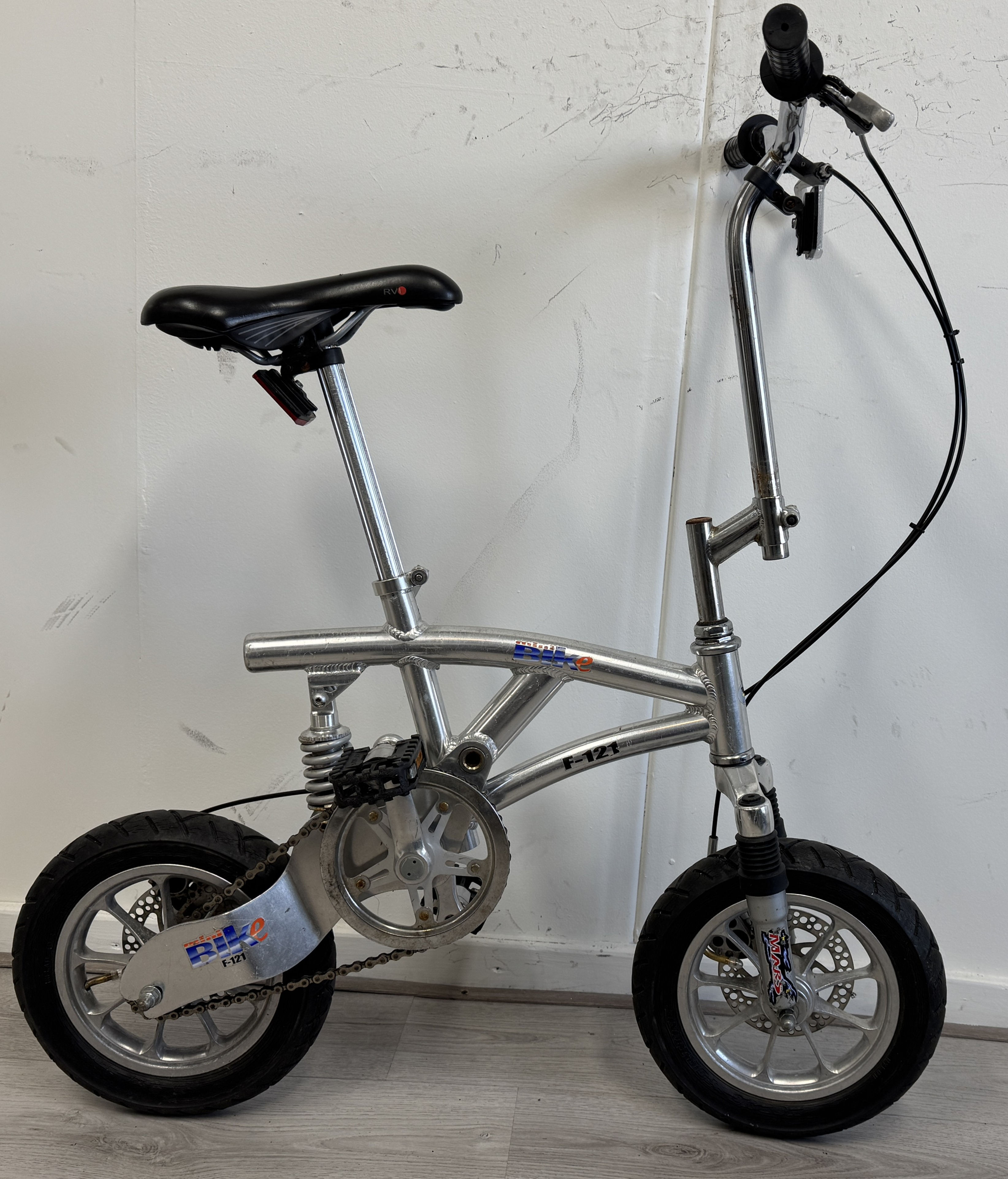 Zilveren opvouwbare fiets in profiel, met zwarte zadel en details.