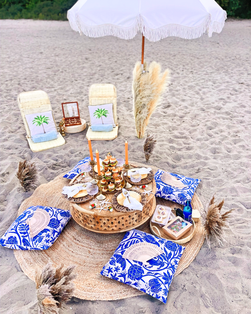 Piknik Bloom, klasyczny na plaży, pod parasolem boho i eleganckie nakrycie stołu z drzewa mango. Perfekcja i lekkość w jednym.