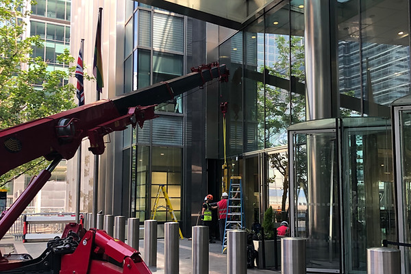 EPP Group engineers installing large exterior glazing using a compact lifting crane at the Barclays Canary Wharf modern commercial building entrance in London.