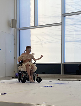 This shows me during a performance in my wheelchair with frilly clown like outfit with blue marks on paper below my feet