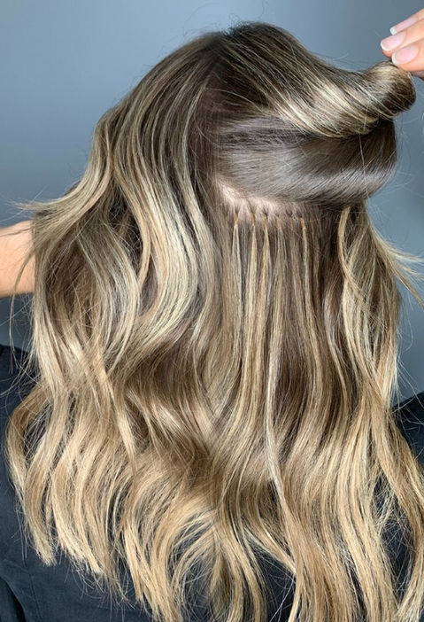 „Dame mit langem blonden Haar von hinten fotografiert, während sie selbst eine Locke im Haar dreht.