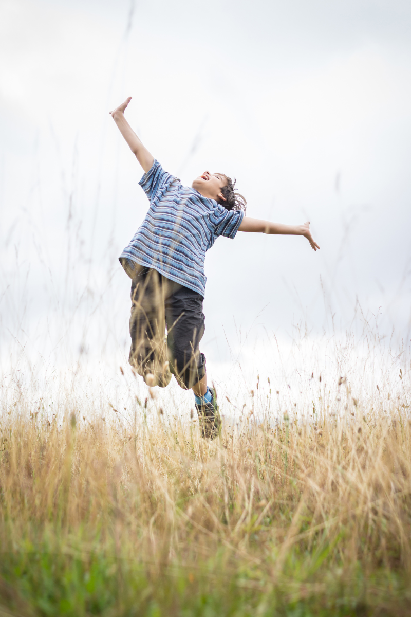 child jumping and smiling in field