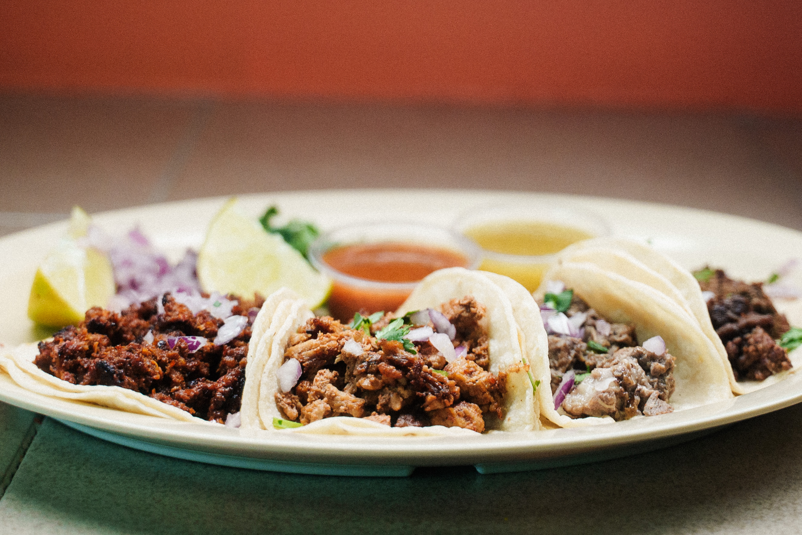Plate of three street tacos with red and green salsa