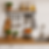 Organização vertical em cozinha compacta com parede de azulejos brancos, prateleira de madeira, barra metálica com utensílios pendurados, facas em suporte magnético, tábuas decorativas, cestos com frutas e temperos, vasos com ervas e bancada de madeira clara ao lado de uma pia inox.