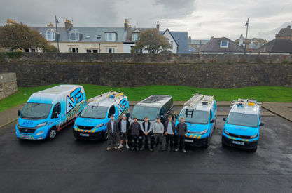 Company team and family standing together in front of fleet of blue vans