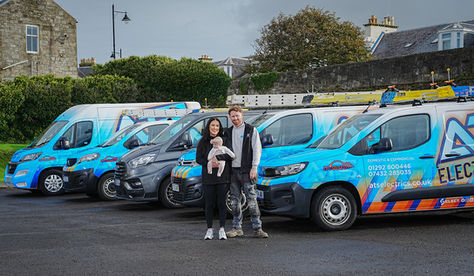 Family standing together in front of fleet of blue electrical service vans