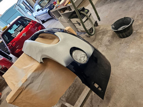 Car bumper partially painted with a headlight, ready for restoration at workshop.