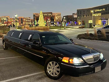 Eye-level view of a sleek black limousine parked outside a festively decorated home at night