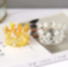 A small golden and silver crown are displayed together on a magazine and a light surface.