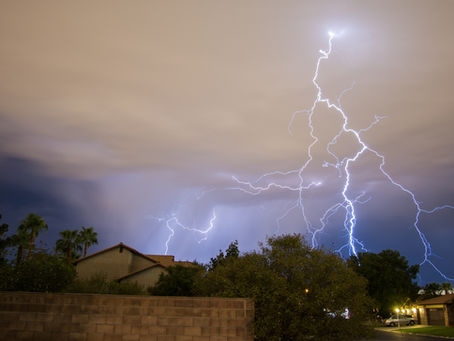 A dramatic lightning storm illuminates the night sky over a suburban neighborhood in Gilbert, AZ, casting an electrifying glow on the homes below.