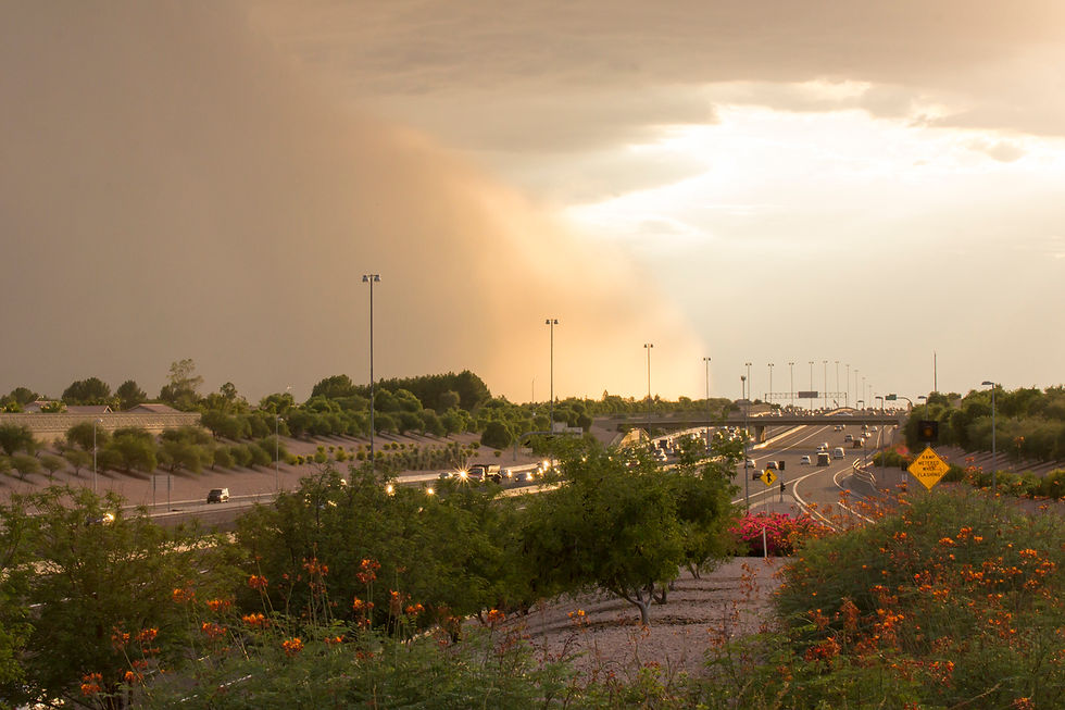 A massive dust storm looms over a busy highway in Mesa, Arizona, casting an orange hue across the landscape as it approaches during dusk.
