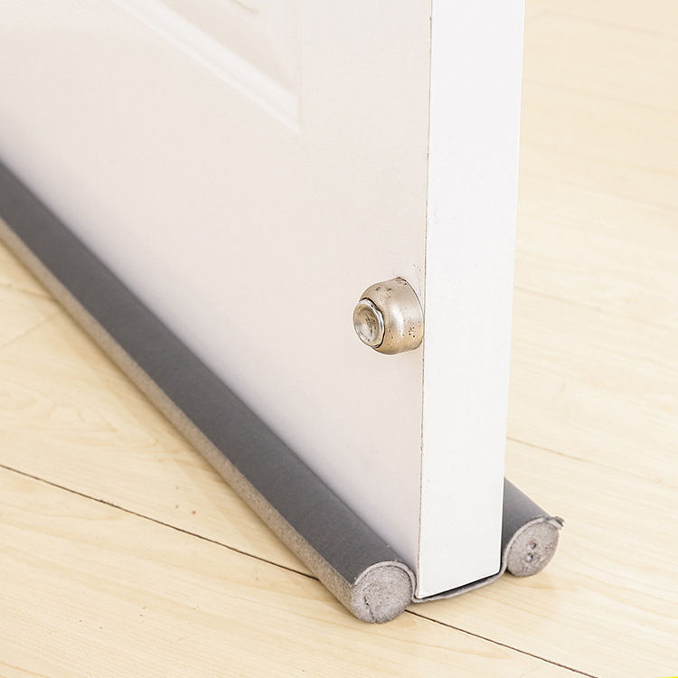 Close-up view of a door bottom seal installed on a wooden door, showing the seal's fit against the floor