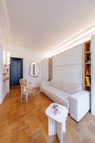 Séjour avec canapé blanc, rangements sur mesure et parquet en bois dans un petit appartement