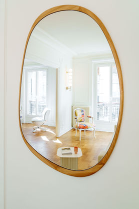 Grand miroir ovale à cadre bois reflétant la salle à manger et la lumière naturelle
