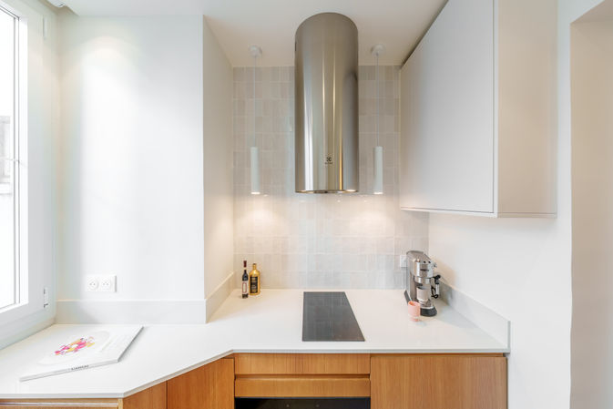 Cuisine contemporaine blanche avec meubles en bois, plan de travail clair et hotte inox