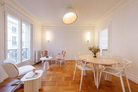 Pièce de vie lumineuse avec salon blanc, fauteuil coloré, table ronde et parquet en bois