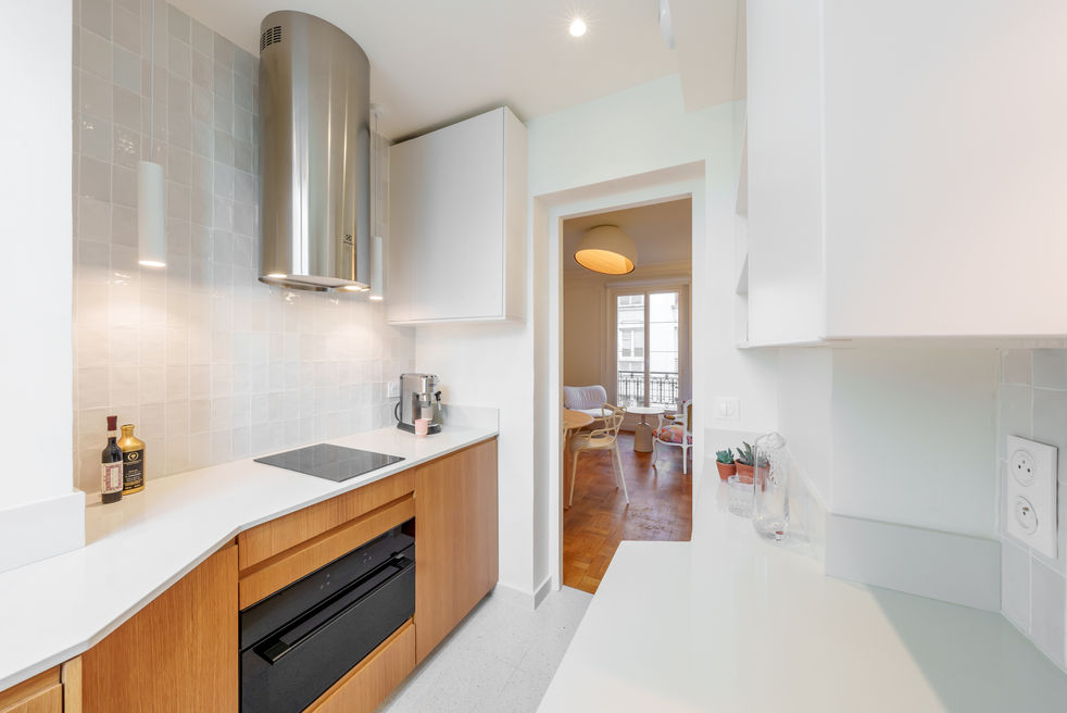 Cuisine blanche et bois avec plaque de cuisson, hotte inox et vue vers la salle à manger