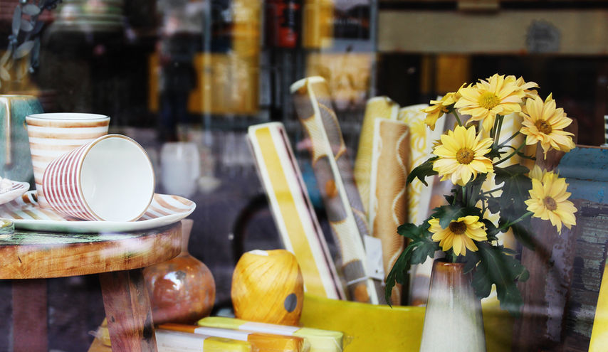Ein Bild von unserem Schaufenster mit Keramikbecher und Teller, Geschenkpapier und Geschenkband und Blumen