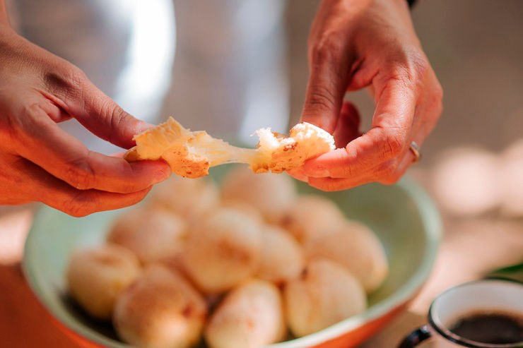 Imagem de uma pessoa com pão de queijo na mão.