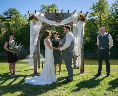 Couple saying their vows under a wooden wedding arbor decorated with flowers