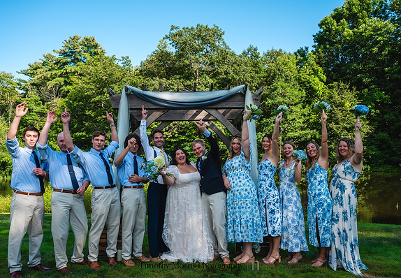 young couple and their bridal party cheering in front of a wedding arch