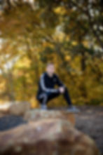 Boy in black sits on rock against fall background