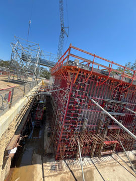 Construction site with red scaffolding, structure and tower in bright daylight.