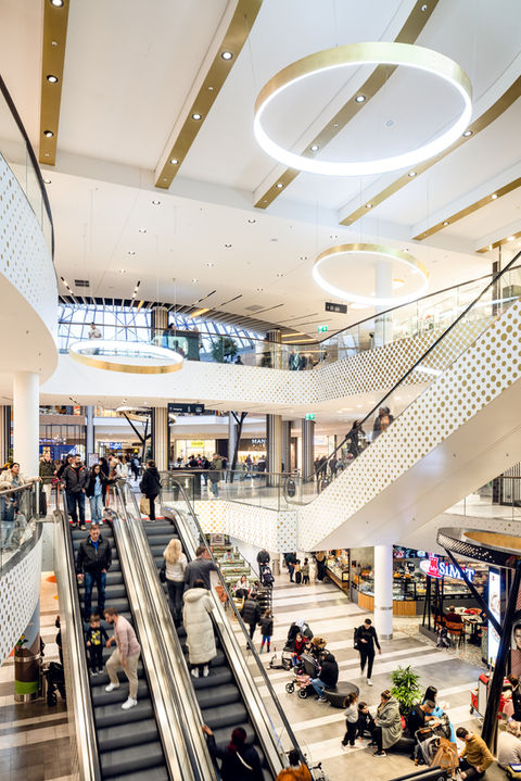 Blick in das Innere eines Shopping-Centers mit Perspektive auf eine Rolltreppe und einigen Personen.
