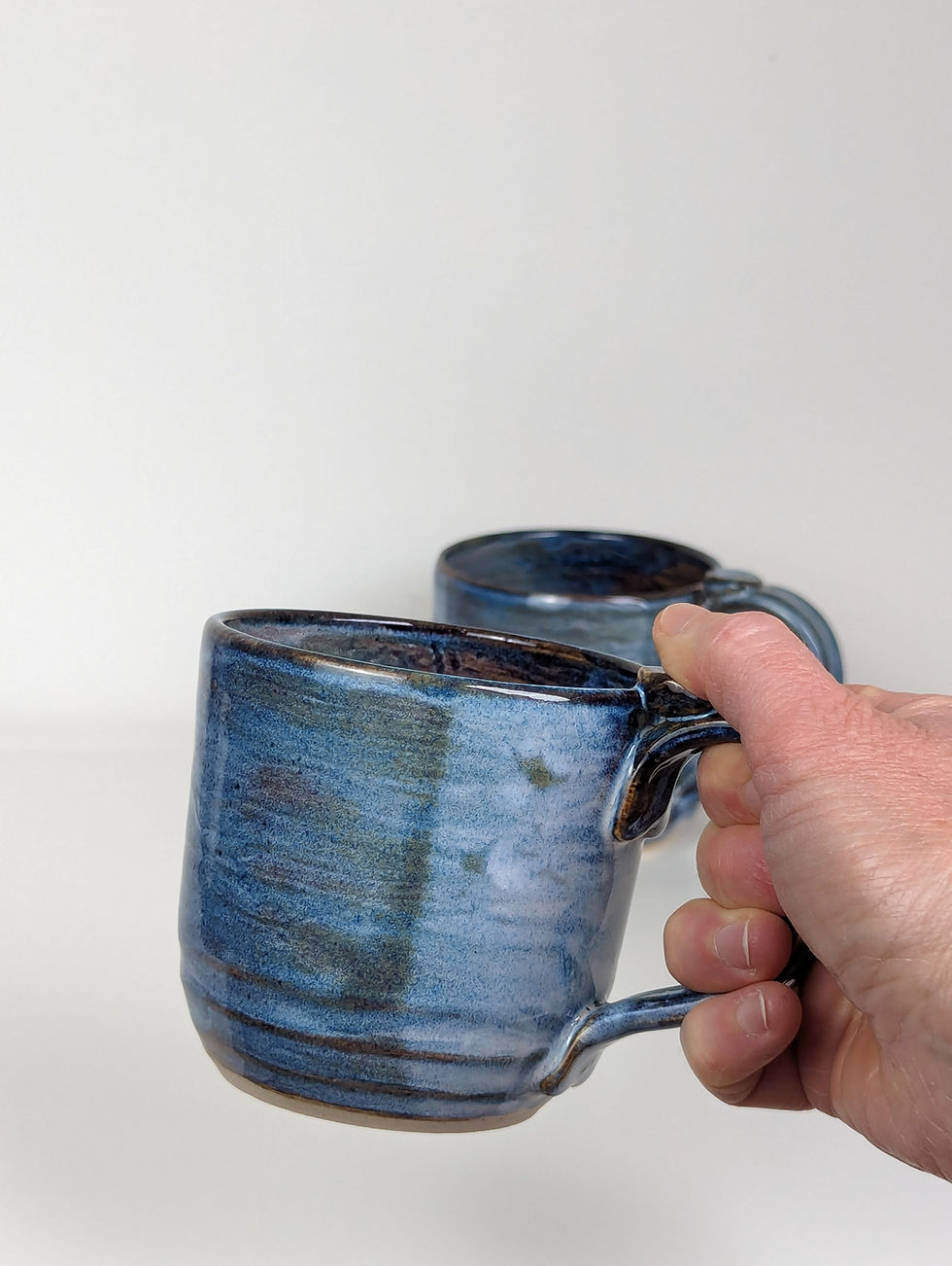 Thumbnail: Large handmade stoneware mugs held in hand, showing the thumbrest and easy‑grip handle.