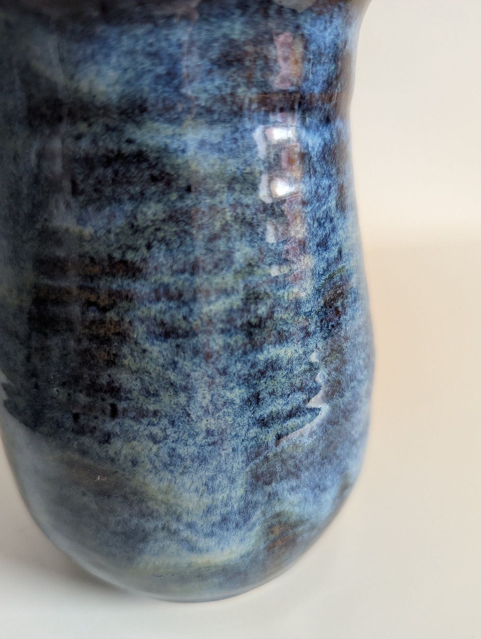 Close‑up of the Stormy Blue glaze on the stoneware vase, showing deep blue tones and warm brown breaks over the curve.