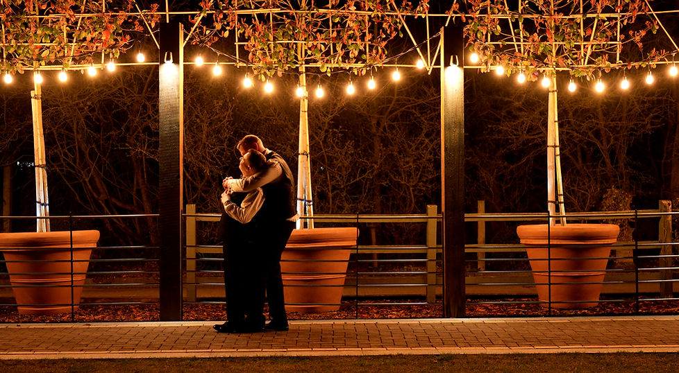 A gay married couple lovingly embracing one another in the soft warm glow of fairy lights.