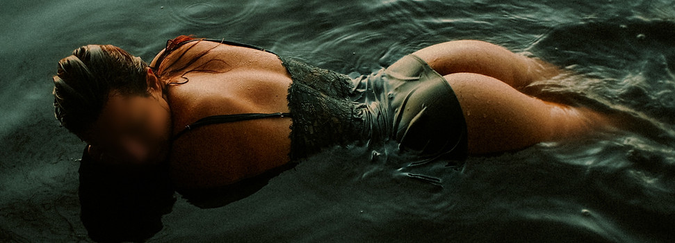 Escort in a green slip just above the water. The ripples form around her tall and hairy figure.