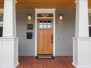 The front door of a house with a covered porch. The door also has small windows at the top and a black door handle.