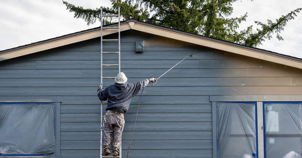 A person wearing protective gear standing on a ladder and spraying paint on the exterior of a house.