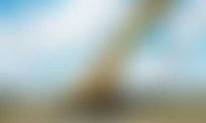 A large, yellow crane with a hook attachment at the end sits in a grassy area outside. It has its stabilizers out.