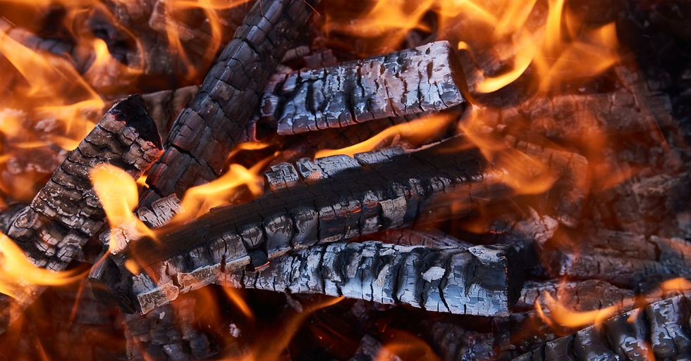 A close-up top view of multiple small wood logs placed on top of each other burning under vivid large flames.